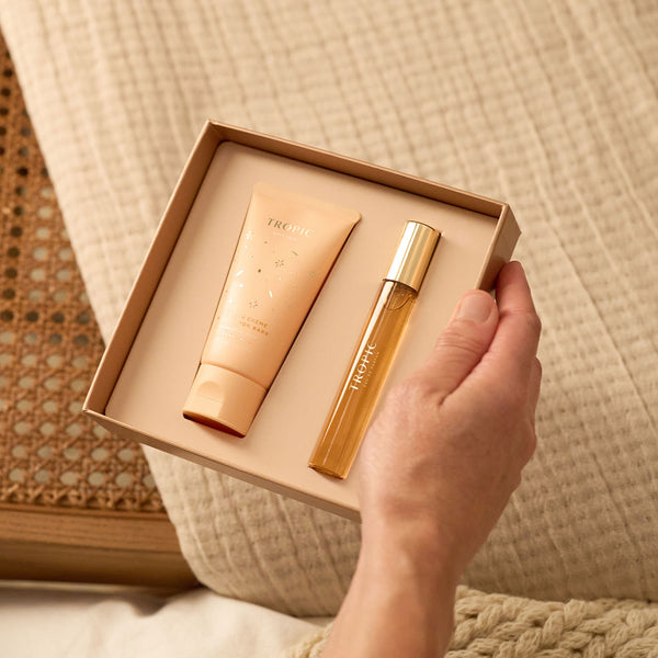 A hand holds a gift box containing the Vanilla Crème & Cinnamon Bark Fine Fragrance and Body Cream Set from Tropic, with a body cream tube and a perfume bottle neatly placed inside.