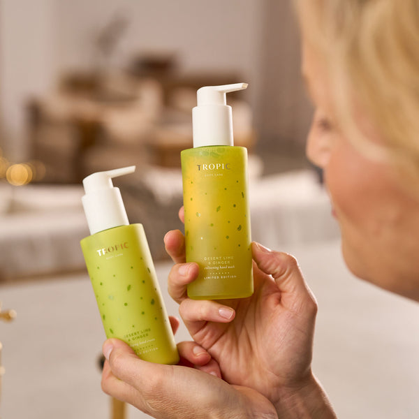 A person holding two bottles from Tropic’s Desert Lime & Ginger Limited Edition collection, including the energising hand wash and enveloping hand cream, both in green pump bottles with a fresh, citrus-inspired design.