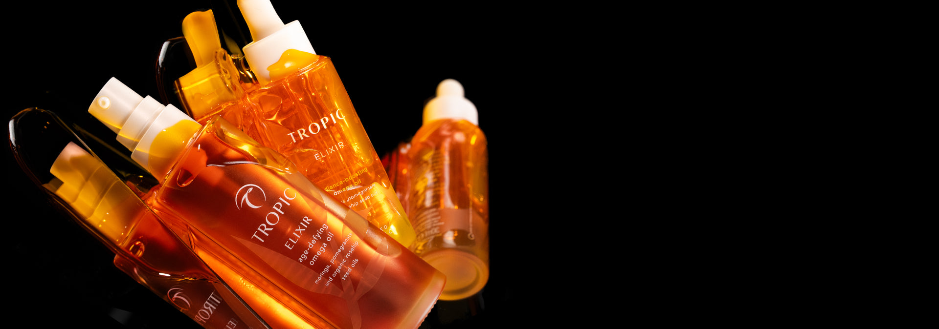 Close-up of Tropic Skincare Elixir bottles glowing in warm amber light, showcasing the rich, golden oils against a black background.