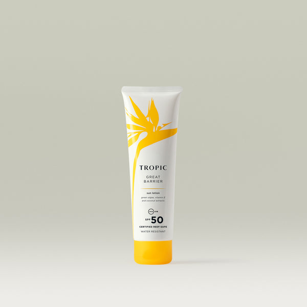 A smaller white tube of Tropic Great Barrier Sun Lotion with SPF 50, decorated with a yellow tropical leaf design and text emphasising 'certified reef-safe' and 'water resistant'.