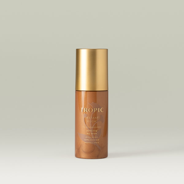 Tropic  Instant Glow perfecting leg serum. See through tube revealing the bronze texture of the product. Subtle leaf design behind the gold text and gold lid.
