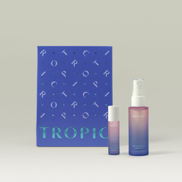 Tropic Skincare gift set titled The Pillow Service – aromatherapy sleep collection, featuring the So Sleepy temple roll-on and pillow mist, displayed in front of a deep blue gift box with metallic detailing.