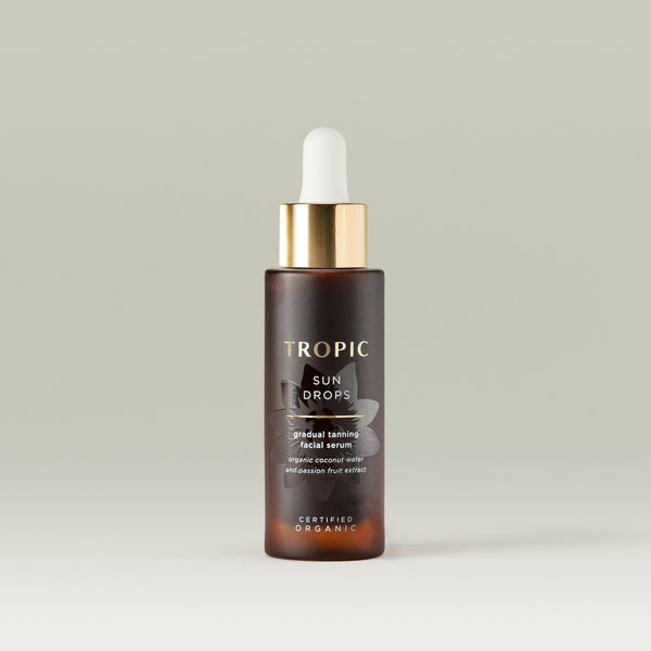 Tropic Sun Drops gradual tanning facial serum. Brown bottle with gold cap and white pipette. A embossed flower behind the text reads: organic coconut water and passion fruit extract. It's certified organic.