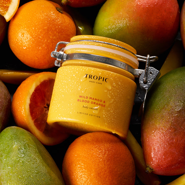 Limited Edition Wild Mango and Blood Orange body smooth placed between mangoes and oranges with water droplets on the jar.
