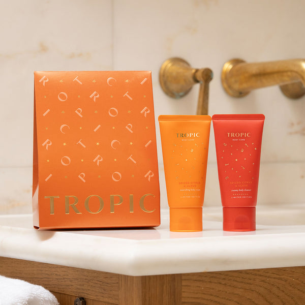Tropic Skincare Spiced Citrus & Clove limited edition gift set with orange and red body care tubes and a matching festive gift box on a bathroom counter.