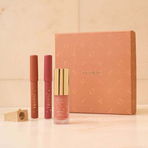 Tropic Skincare Lip Service gift set featuring two lip pencils, a Lip Silk plumping serum, and a sharpener, displayed with a peach-coloured festive gift box.