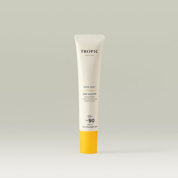Tropic Sun Day dewy facial SPF 50 sunscreen in a sleek white tube with a bright yellow cap, displayed against a soft neutral background.