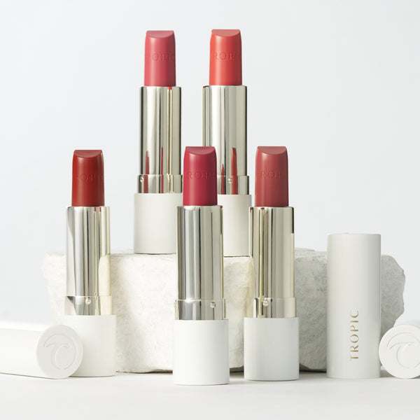 Five Tropic Butter Tints in varying shades displayed upright on a white block, with caps placed beside them.