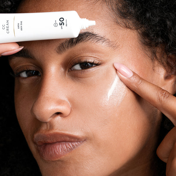 Woman applying CC cream to her face with a focus on the product.