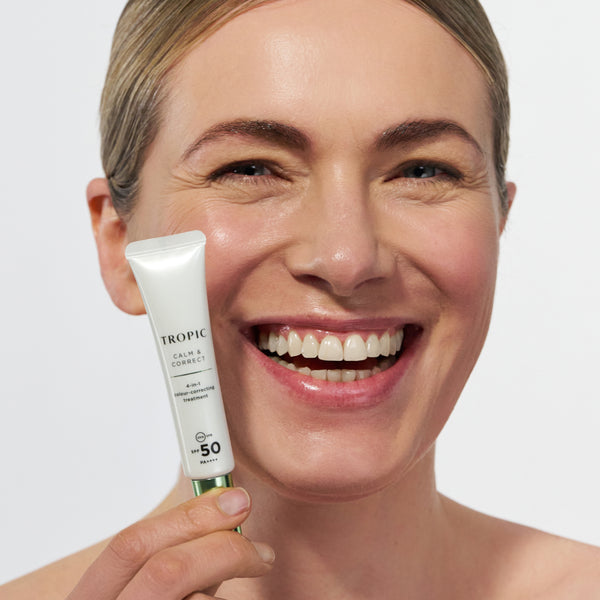 Smiling person holding Tropic Calm & Correct SPF 50 colour-correcting treatment.