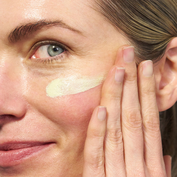 Close-up of a person applying a light green skincare cream to their cheek.