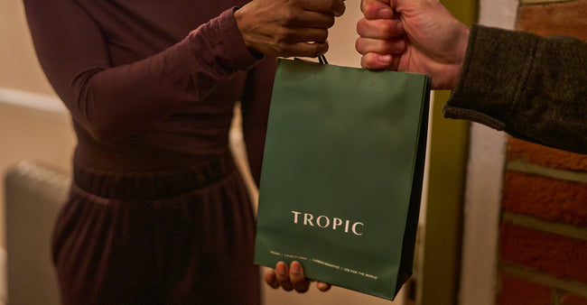 Two people holding a green paper bag labelled 'Tropic' between them.