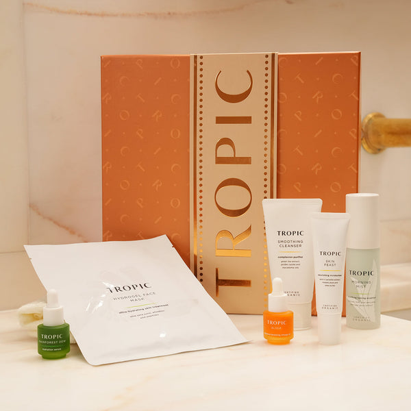 Tropic Skincare Facial Faves gift set featuring Smoothing Cleanser, Skin Feast, Morning Mist, Elixir, Rainforest Dew serum, and Hydrogel Face Mask displayed with a festive orange gift box.