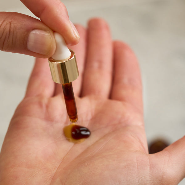 Close-up of a model using Tropic Sun Drops, dispensing the tanning serum into her hand with a dropper.