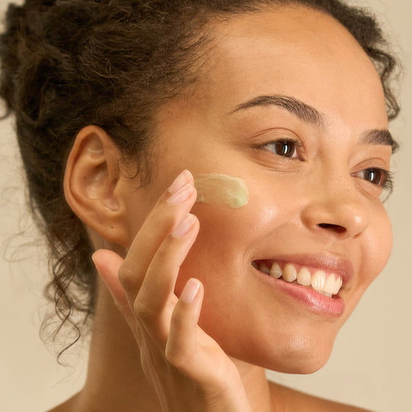 Smiling woman applying Tropic Skincare product to her cheek, showcasing the Dewy Skin Collection.