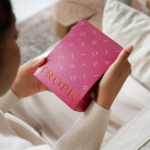 A person holds a pink gift box with gold lettering labelled 'TROPIC,' containing The Soft Touch Treatment Hand and Lip Duo.