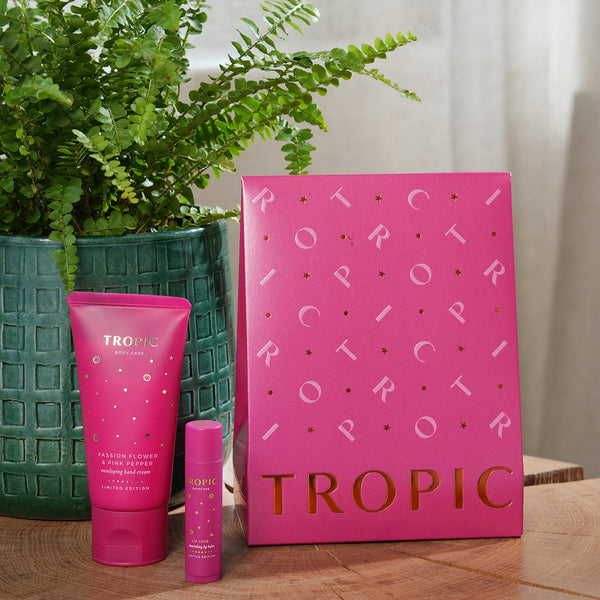 The Soft Touch Treatment collection by Tropic. A vibrant pink gift set box displayed with two matching products: Passion Flower & Pink Pepper hand cream and Limited Edition Lip Love nourishing balm.