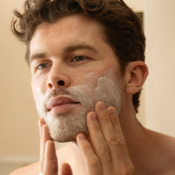 A man with short curly hair applies Look Sharp sensitive shave to his face, gently massaging it into his cheeks.