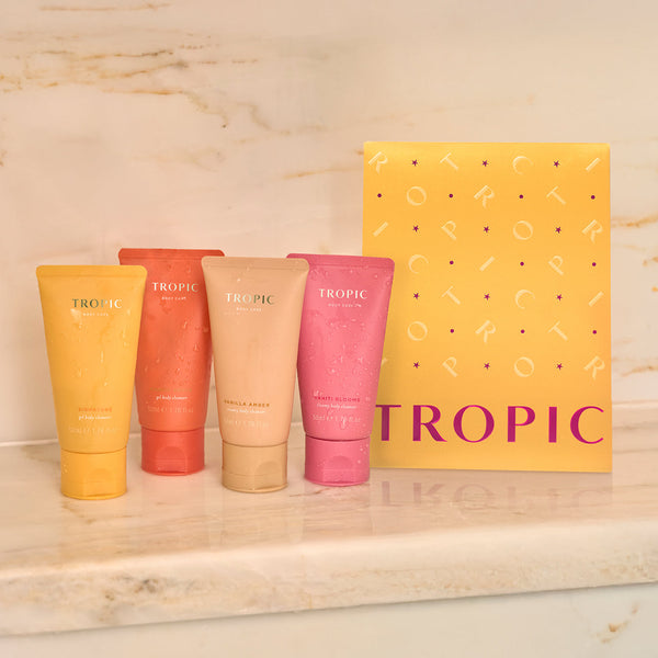 Tropical Showers - transportive body wash set by Tropic. A bright yellow gift set box with four colourful mini body washes displayed in front: Signature, Mango Grove, Vanilla Amber, and Tahiti Blooms.