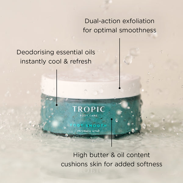 Foot Smooth Enzymatic Scrub jar in aqua glass with white lid, splashed with water droplets. Overlay text highlights: “Dual-action exfoliation for optimal smoothness”, “Deodorising essential oils instantly cool & refresh”, and “High butter & oil content cushions skin for added softness.”