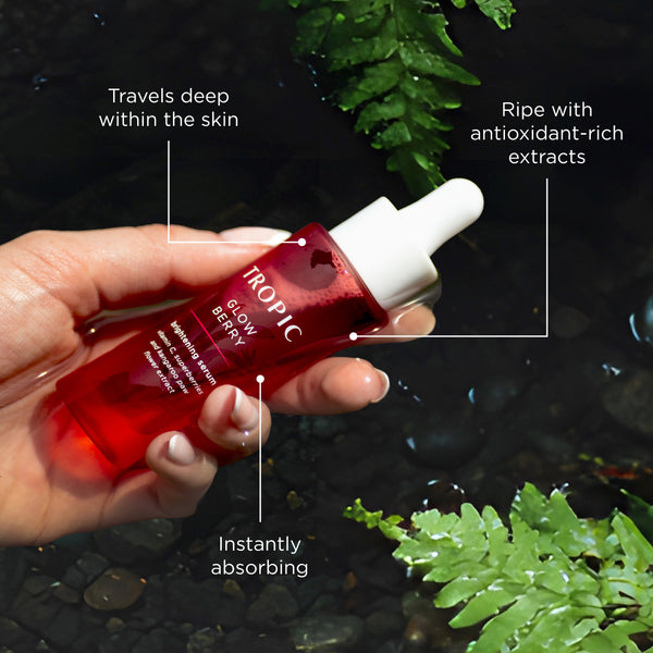 Hand holding Tropic Glow Berry brightening serum over water with text highlighting travels deep within the skin, antioxidant-rich extracts, and instant absorption.