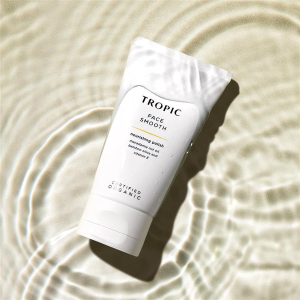 Tropic Face Smooth nourishing polish tube with macadamia nut oil, bamboo silica, and vitamin E, placed in rippling water for a refreshing look.