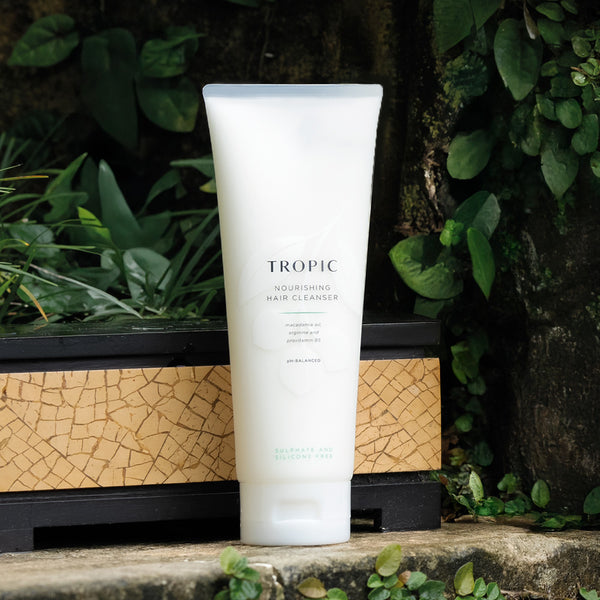 Nourishing hair cleanser contains macadamia oil, arginine and provitamin B5. Its presented in a white squeeze tube with lid and there is a faint floral design on the bottle. 
It is sulphate and silicone free.
It rests against a leaf background.