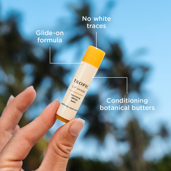 Close-up of Tropic Lip Shade nourishing SPF 50 balm held outdoors, highlighting its glide-on formula, no white traces, and conditioning botanical butters.
