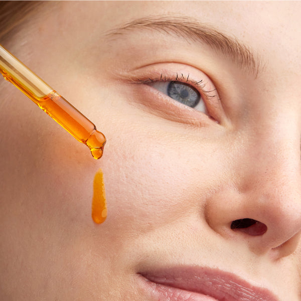 This image shows a close-up of a person applying Elixir, a radiance-boosting omega oil, to their cheek using a dropper. The golden hue of the oil reflects its rich, nourishing formula packed with essential omegas. The product is designed to deeply hydrate and enhance the skin's natural glow, leaving it smooth and radiant.