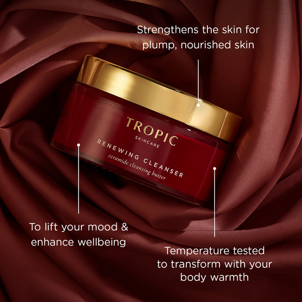 Renewing Cleanser in a red jar with a gold lid, set on rich red fabric. On image text highlights: “Strengthens the skin for plump, nourished skin”, “To lift your mood & enhance wellbeing”, and “Temperature tested to transform with your body warmth”.