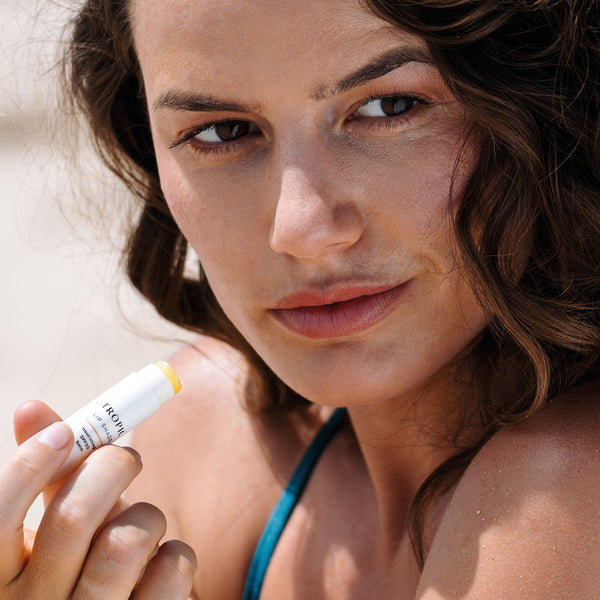 Woman holding Tropic Lip Shade, ready to apply the nourishing balm for sun protection and hydration.
