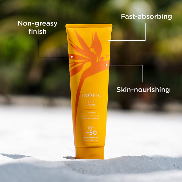 Tropic Skin Shade Sun Cream SPF 50 tube on sandy beach with labels highlighting its non-greasy finish, fast-absorbing, and skin-nourishing properties.