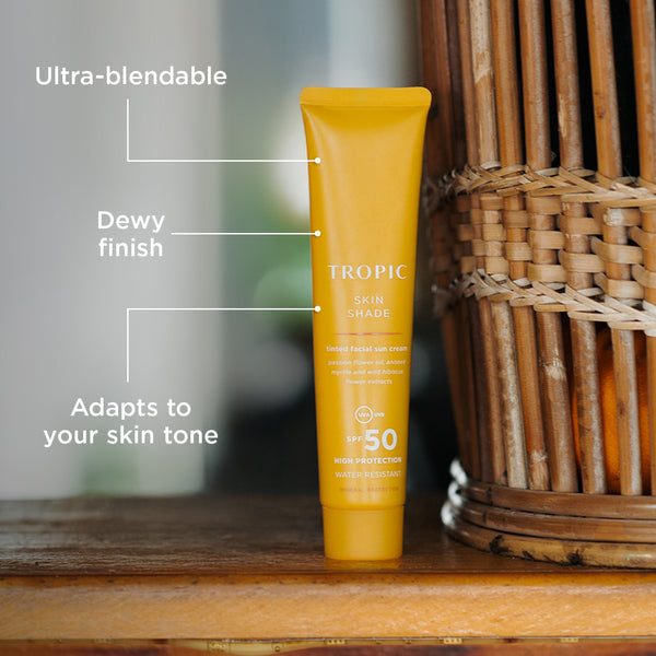 Tropic Skin Shade tinted facial sun cream SPF 50 tube standing upright on a wooden surface, with text highlighting its ultra-blendable, dewy finish and skin tone adaptability.