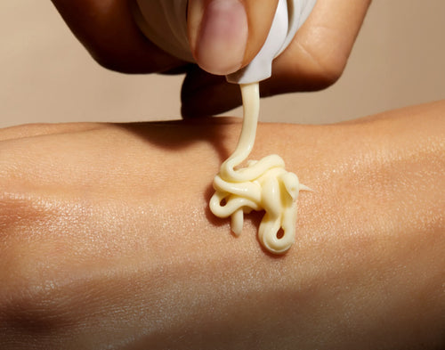Hand applying cream to a person's arm with a neutral background