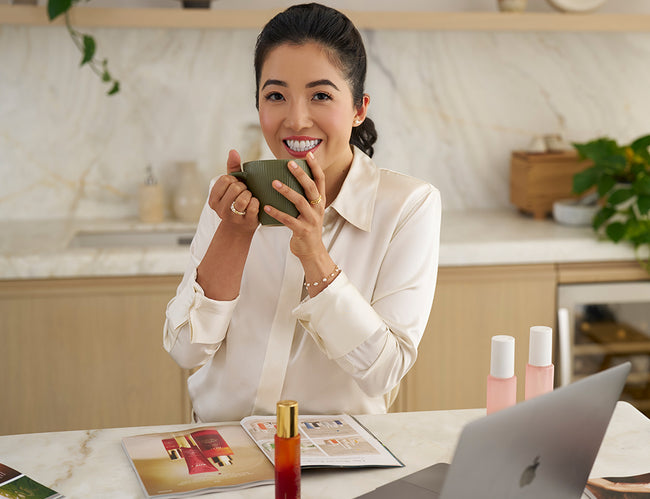 CEO and Founder Susie Ma holding a mug in a kitchen with a laptop and magazines on the table.