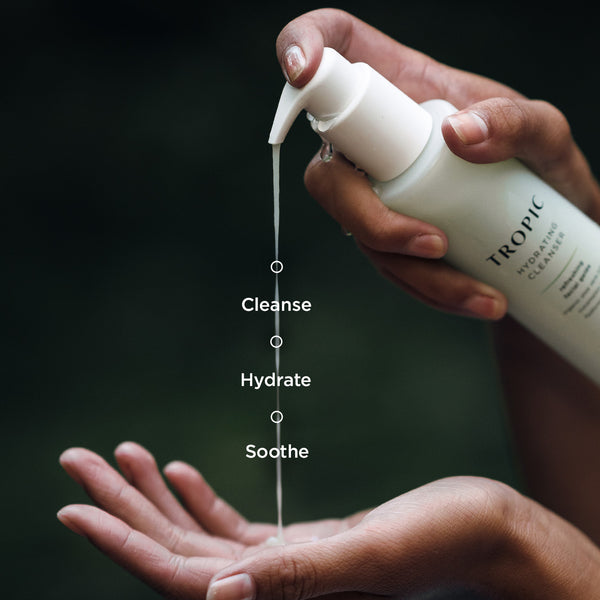 Close-up of hands dispensing Tropic Hydrating Cleanser from a pump bottle, with text overlay reading 'Cleanse,' 'Hydrate,' and 'Soothe' along the stream of product.