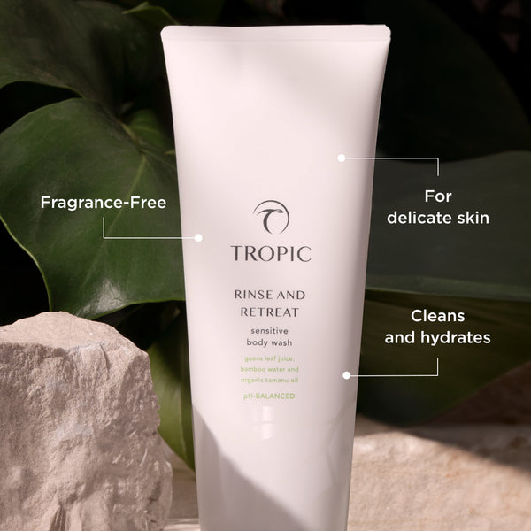The image showcases a tube of Tropic Rinse and Retreat Sensitive Body Wash placed against a natural backdrop with soft lighting. The product highlights include:

Fragrance-Free, suitable for those with sensitivities.
For delicate skin, emphasizing its gentle formulation.
Cleans and hydrates, offering both cleansing and moisturizing benefits.
The label mentions key ingredients such as guava leaf juice, bamboo water, and organic tamanu oil, and notes that it is pH-balanced, ensuring skin-friendly care. 