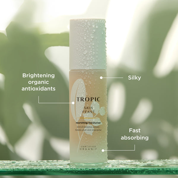 This image features a bottle of Skin Feast, a nourishing moisturiser. Key attributes are highlighted:

Brightening organic antioxidants for skin protection and radiance.
Silky texture for a luxurious application.
Fast absorbing formula to deliver instant hydration.
The product contains ingredients like bird of paradise extract, Kakadu plum extract and shea butter.  The dewy aesthetic emphasises its hydrating and refreshing properties.