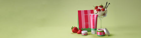 Banner-style image showcasing the Very Berry & Vanilla Velvet collection from Tropic. A striped gift set box, body lotion, body scrub and lip treatment are grouped with ripe strawberries and a glass dessert layered with cream and vanilla. The arrangement sits on the right against a soft pistachio-green backdrop, leaving open space across the left side of the image.