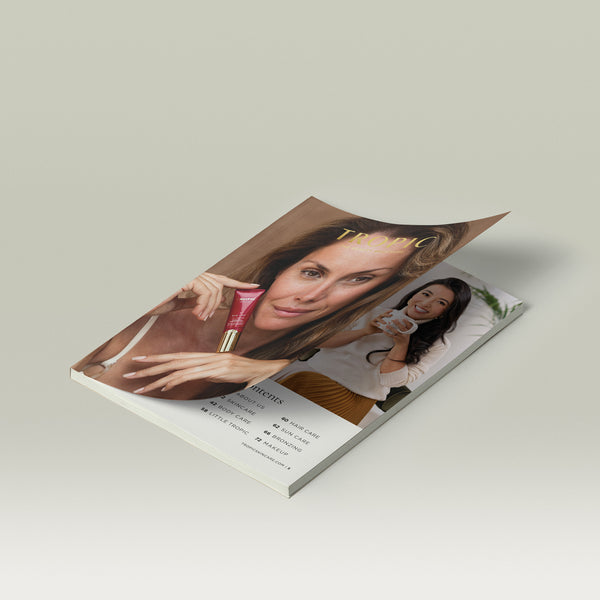 Tropic Skincare beauty brochure lying partly open on a white surface, featuring a woman holding red Eye Lift product on the cover and another woman smiling with a skincare jar inside.