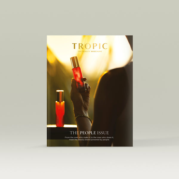 Tropic Beauty Brochure cover featuring a hand holding a glowing red Youth Potion Advanced serum bottle in warm sunset light, with a softly lit product display in the background.