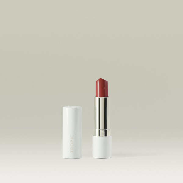Butter Tint Lip & Cheek Balm in shade Confident by Tropic. The product is displayed standing upright with the cap removed and placed beside it, revealing a deep pink balm in a sleek white and silver tube against a soft neutral background.