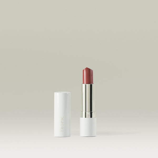 Butter Tint Lip & Cheek Balm in shade Natural by Tropic. The product is shown upright with the lid removed and placed beside it, revealing a soft rose-pink balm in a sleek white and silver tube against a neutral background.