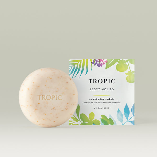 Tropic Zesty Mojito Cleansing Body Pebble – a round, exfoliating soap bar with natural flecks, embossed with the Tropic logo, alongside its vibrant tropical-themed packaging. Made with shea butter, golden jojoba oil, and coconut cleansers for a pH-balanced cleanse.