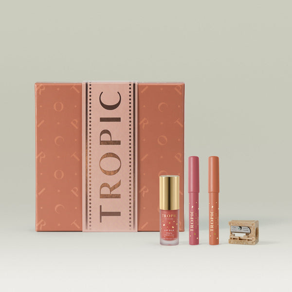 Tropic Skincare gift set titled The Enhancing Lip Service – sculpt and define trio, featuring Lip Silk conditioning serum, two lip crayons in complementary shades, and a sharpener, displayed alongside a rose-toned gift box.