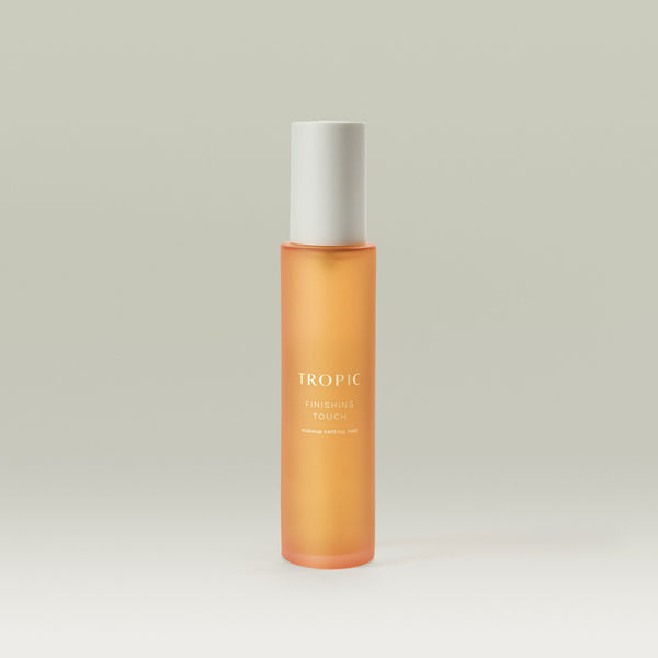 Tropic Finishing Touch makeup setting mist in a sleek orange frosted bottle with white cap, standing upright on a neutral background.