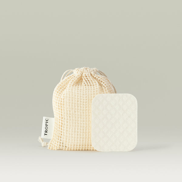 Tropic Forest Leaves Water-Activated Facial Pads shown with a textured pad in front of a cream-colored drawstring mesh bag labelled with the Tropic logo, displayed on a neutral background.
