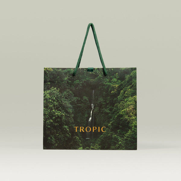 Tropic Skincare reusable gift bag with rainforest design and green rope handles, featuring a waterfall image and the Tropic logo in gold.