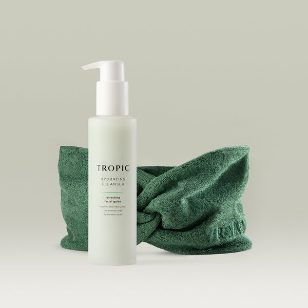 Tropic Hydrating Cleanser bottle with pump dispenser displayed in front of a green bamboo headband on a neutral background.