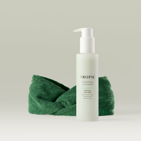 Tropic Hydrating Cleanser bottle with pump dispenser displayed in front of a green bamboo headband on a neutral background.